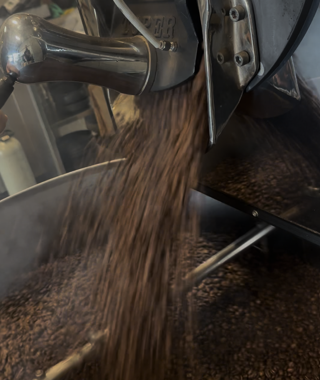 Hands operating the Toper coffee roaster at King Carlos Coffee Hurstville, beans cascading from the drum