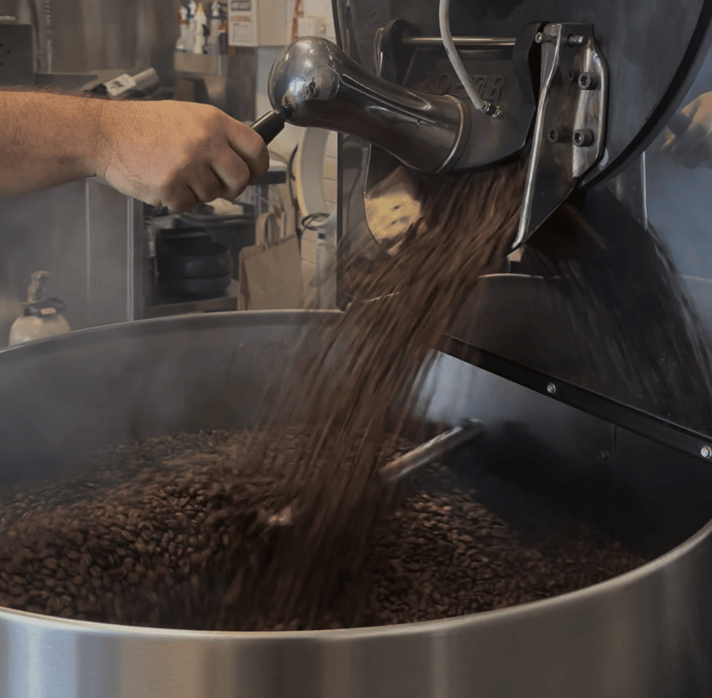 Hands operating the Toper coffee roaster at King Carlos Coffee Hurstville, beans cascading from the drum